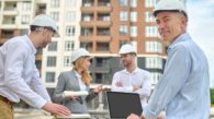Smiling contented middle-aged engineer posing for the camera with his colleagues on the background