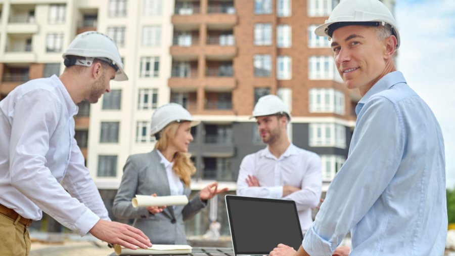 Smiling contented middle-aged engineer posing for the camera with his colleagues on the background