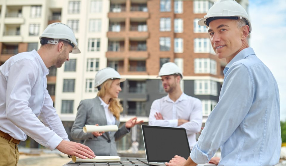 Smiling contented middle-aged engineer posing for the camera with his colleagues on the background